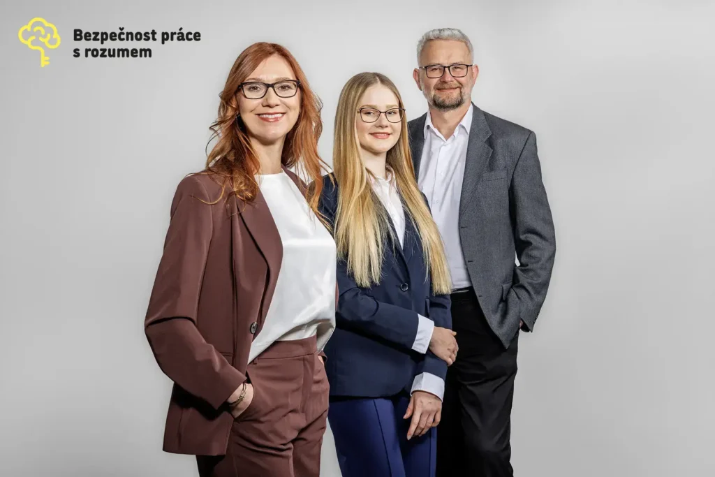 Tři lidé v business oblečení pózují před šedým pozadím s logem Bezpečnost práce s rozumem.