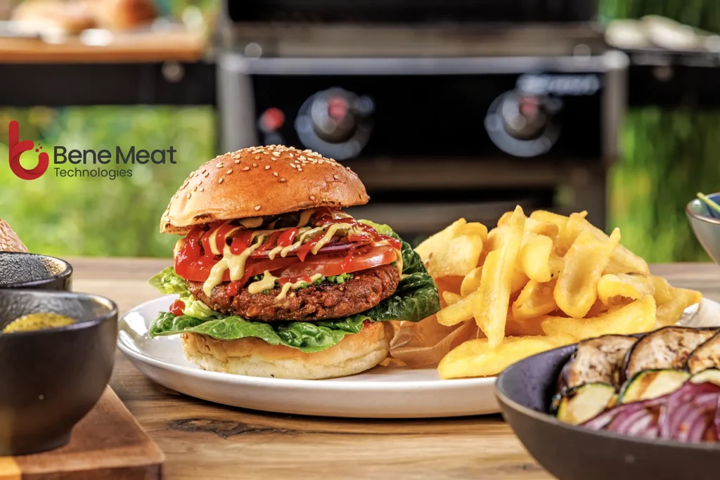 Burger se zeleninou, hranolky a logo Bene Meat Technologies na stole venku